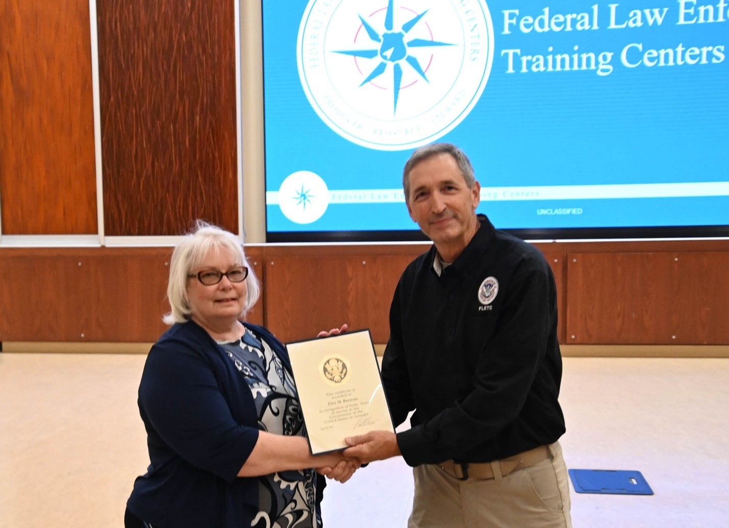 Federal Law Enforcement Training Centers Director Benjamine C. Huffman presents Disability Program Manager Elise Burtrum with a 40-Year Time in Service Certificate in Artesia, NM, Sep. 25, 2024. (Henry Rolon/FLETC OPA)